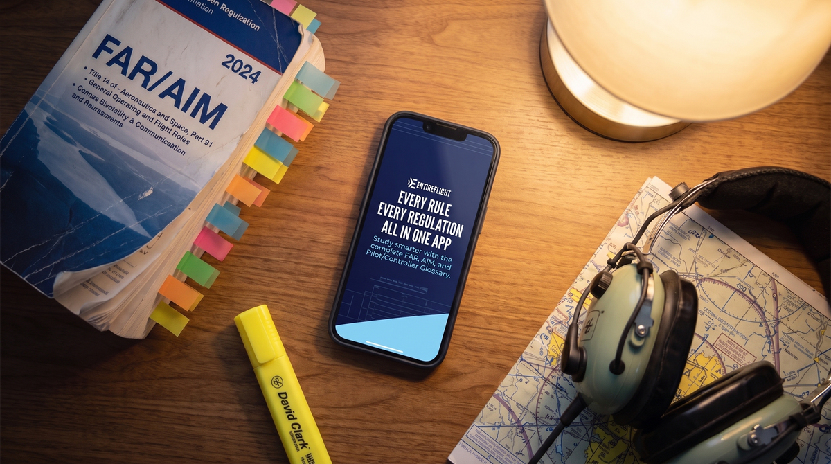 EntireFlight FAR/AIM app on a smartphone next to a tabbed printed FAR/AIM book, aviation headset, and sectional chart on a student pilot's study desk